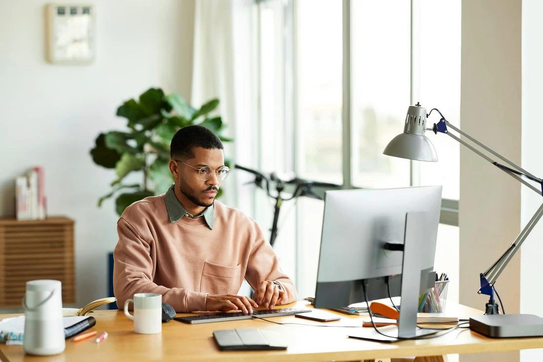 A man working calmly at a bright desk by large windows